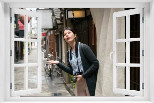 asian female traveler with camera looking up at sky and reaching out hand to see if itâs raining outside of Japanese restaurant in a tradition alleyway near nanba-eki Osaka japan