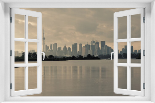 Fototapeta Naklejka Na Ścianę Okno 3D - Autumn day view across inner bays of Lake Ontario in Tommy Thompson Park with foggy Downtown Toronto skyline under grey cloudy skies in background with water surface reflecting the buildings outlines
