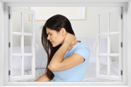 Young woman suffering from neck pain on bed in bedroom