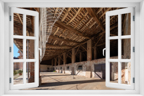 Fototapeta Naklejka Na Ścianę Okno 3D - Old stable with old abandoned barn under large porch of wooden beams and roof tiles typical of the countryside in the province of Cuneo, Piedmont, Italy