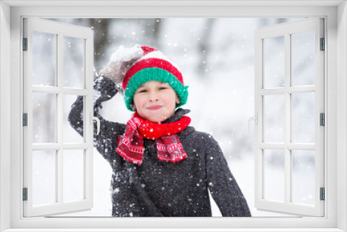 Funny little boy in winter clothes walks during a snowfall. Winter outdoor activities for children. A cute child in a warm hat rejoices at the first snow.