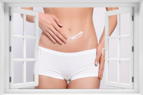 Woman applying body cream onto her belly against white background, closeup