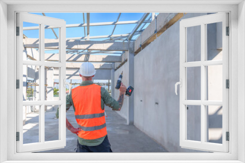 Male engineer wearing safety suit and hard hat holding toolbox and electric drill in construction site for building site survey in civil engineering project.