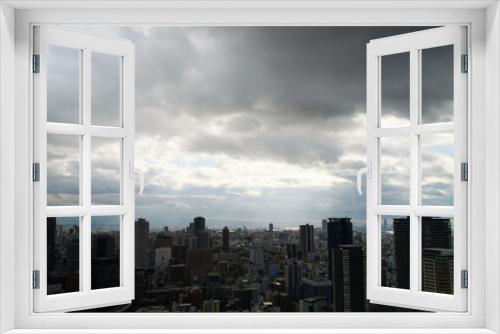 Overhead view of Osaka's Umeda area from a hill on a cloudy day, sunlight shining through a gap in the clouds.