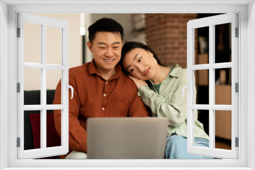 Loving asian couple using laptop together, surfing internet or watching movie online, wife leaning on husband's shoulder