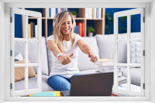 Young blonde woman studying using computer laptop at home approving doing positive gesture with hand, thumbs up smiling and happy for success. winner gesture.