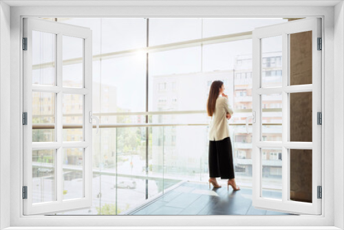 Full length of thinking businesswoman looking the city through window