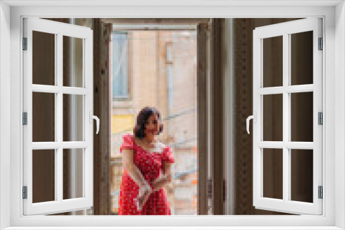 a beautiful and happy brunette women in red retro dress in the balcony doorway 