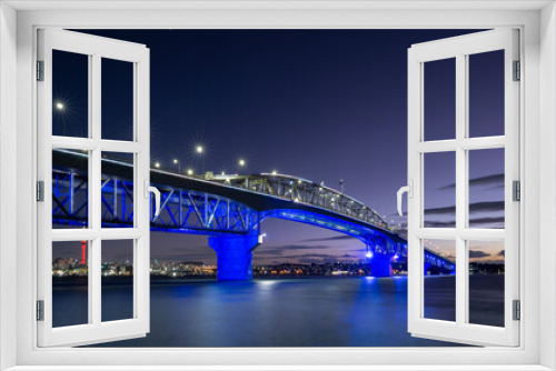 Fototapeta Naklejka Na Ścianę Okno 3D - Auckland Harbour Bridge glowing in blue. Skytower in gold and red. Auckland, New Zealand