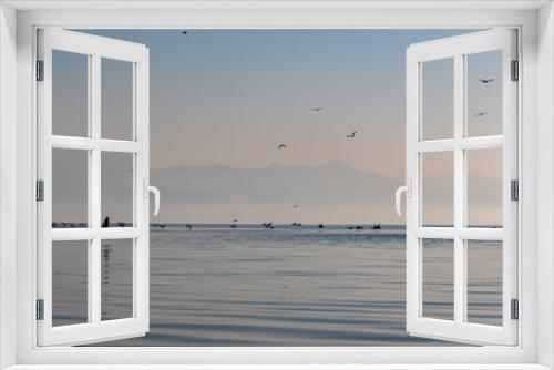 Fototapeta Naklejka Na Ścianę Okno 3D - Silhouette of flock of birds flying over water surface at sunrise at Lake Skadar near Virpazar, Bar, Montenegro, Balkans, Europe. Water reflection with misty Dinaric Alps mountains. Freedom concept