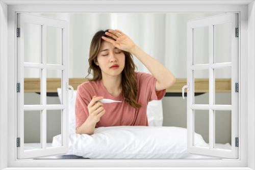 Young asian woman taking temperature with digital thermometer while sitting in bed. Covid-19 infected people stay in their rooms alone for safety, not infect people in the house.