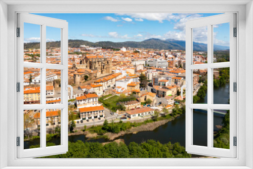 View from drone of residential area of Plasencia city with brownish tiled roofs of houses and ancient gothic roman catholic cathedral on green bank of meandering Jerte river in spring, Caceres, Spain