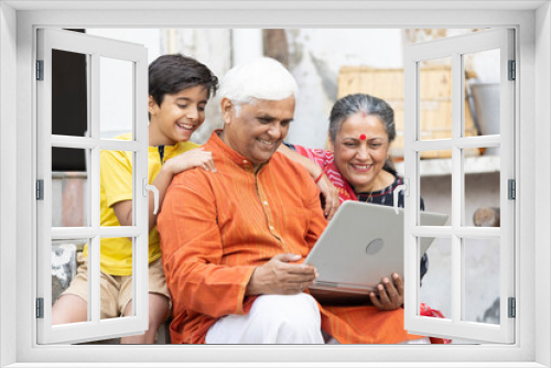 Indian rural family using laptop at home with grandson.