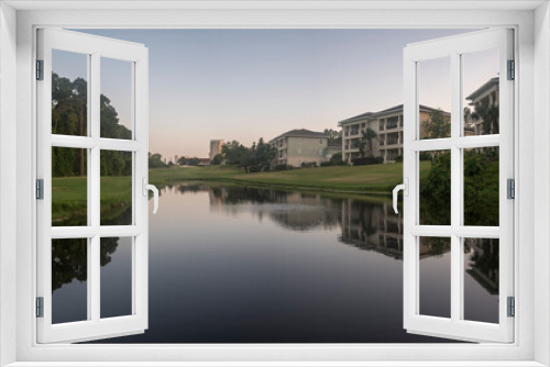 Fototapeta Naklejka Na Ścianę Okno 3D - Lake with reflections of the residential buildings near the shore at Destin, Florida. Three-storey residential buildings with balconies and lakefront views with grass and trees on the shore.