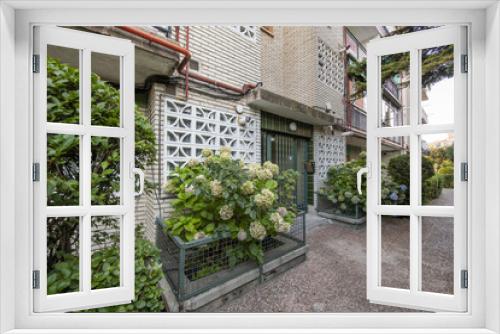 Fototapeta Naklejka Na Ścianę Okno 3D - Portal of a building with white bricks, a green metal door and flower pots full of flowers