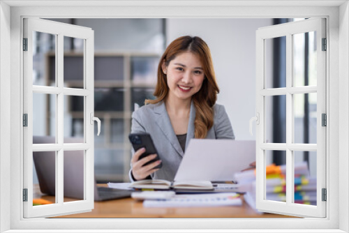 Smiling young Asian business woman executive looking at smartphone using cellphone mobile cell tech, happy ethnic professional female worker working in office typing on cellphone sitting at desk.