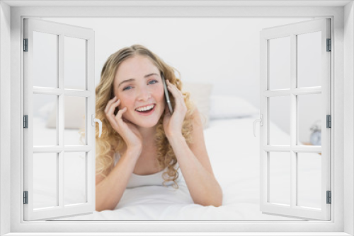 Pretty smiling blonde lying on bed phoning