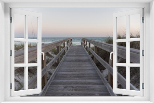 Fototapeta Naklejka Na Ścianę Okno 3D - Straight wooden pathway with railings in between sand dunes against the ocean and horizon sky. Wooden walkway near the protected sand dune with grasses with views of ocean waves in Destin, Florida.