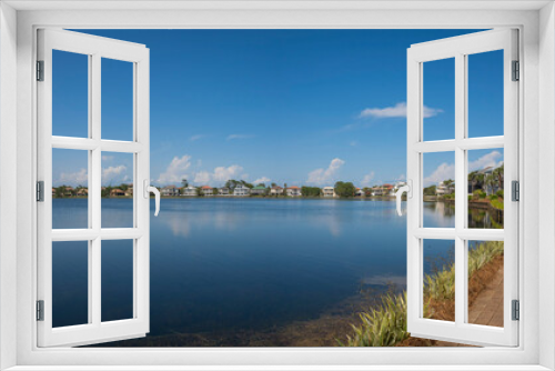 Fototapeta Naklejka Na Ścianę Okno 3D - View of Four Prong Lake from a bricks pathway near the residences at Destin, Florida. Panorama of lakefront houses with pathway at front and blue sky background.