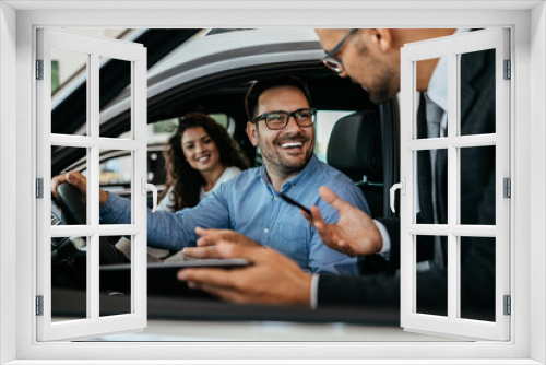 Middle age couple choosing and buying car at car showroom. Car salesman helps them to make right decision.