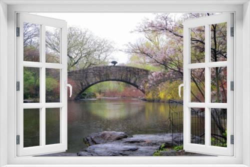 Fototapeta Naklejka Na Ścianę Okno 3D - spring rain showers over a rustic stone bridge and pond in central park with blossiming flowers and a single figure