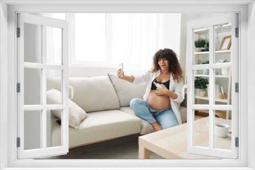 A pregnant woman blogger advertises a cream for pregnant women from stretch marks on the body during pregnancy filming herself on the phone while sitting on the couch at home freelancer