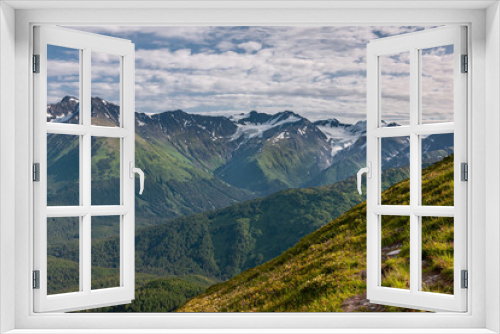 Fototapeta Naklejka Na Ścianę Okno 3D - Girdwood Alaska, USA - July 23, 2011: Chugach Park. Yellow-green weeds on mountain flank in front of wide landscape of mountain range with snow patches under blue cloudscape. Green forests