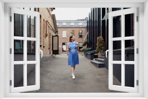 Busy modern pregnant woman walking among office buildings using a smartphone. Woman in a blue vintage dress and white purse using phone on the go