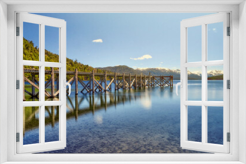Fototapeta Naklejka Na Ścianę Okno 3D - A beautiful pier to the left of the lake in shades of green and blue with a background of mountains in the morning.