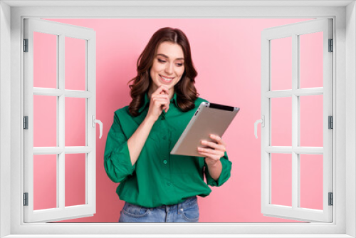 Photo of minded intelligent smart woman with wavy hairdo dressed green shirt look at tablet choose product isolated on pink background