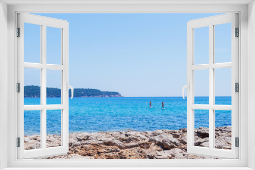 Fototapeta Naklejka Na Ścianę Okno 3D - A couple standup paddleboarding on the beautiful blue sea under a clear summer sky, enjoying a tranquil day of leisure and recreation. Panoramic view.