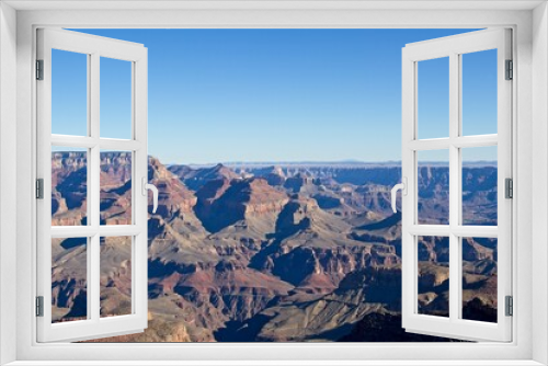 Fototapeta Naklejka Na Ścianę Okno 3D - Bright desert sunlight shines down on the Grand Canyon, casting shadows on every crease and layer of the eroded canyon carved over many years by the Colorado River thousands of feet below