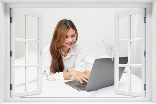 Woman in white nightgown waking up on weekend morning resting and relaxing playing with laptop mobile phone Eating bread and drinking tea in glass inside white bedroom.  Morning vacation concept.