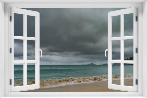 Fototapeta Naklejka Na Ścianę Okno 3D - Rainy seascape. Low gray clouds in the sky. The waves of the turquoise ocean are foaming on the sandy beach. A green hill and islands on the horizon. Seychelles. Mahe