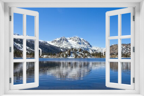 Fototapeta Naklejka Na Ścianę Okno 3D - Snow tops the Sierra Nevada Mountains from the crystal clear waters of June Lake, which sits at the bottom of the mountain range's steep eastern escarpment