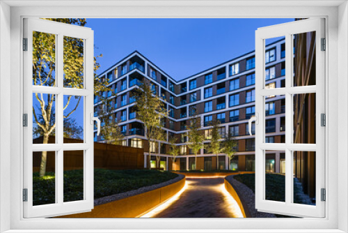 Fototapeta Naklejka Na Ścianę Okno 3D - Budynki mieszkalny w europejskim mieście nocą. Nowoczesne bloki. Dziedziniec z roślinnością i oświetleniem. Wykończenie z blachy rdzawej, corten. Garaż podziemny

