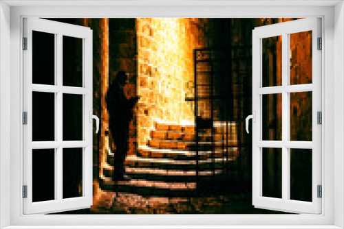 Fototapeta Naklejka Na Ścianę Okno 3D - A man stands in the dark on an ancient stone street in Jaffa. Night, the lights are on and the window is lit. Israel, Tel Aviv.