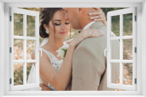 Wedding portrait photo. Groom in a light suit. The bride and groom are standing in the forest embracing. Beautiful makeup and hair. Couple in love. Summer light. The shadows