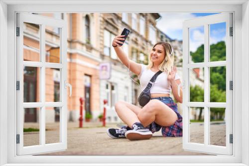 Hipster influencer teenager girl with headphones on her head sitting on a skateboard on a city walking street and taking a selfie with her smartphone - Outdoor youth culture concept