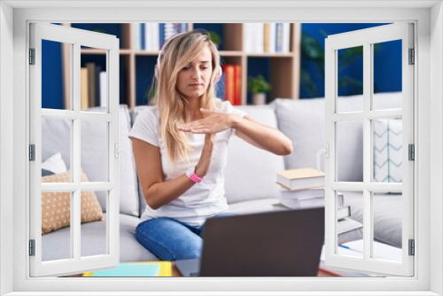 Young blonde woman studying using computer laptop at home doing time out gesture with hands, frustrated and serious face