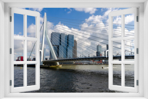Fototapeta Naklejka Na Ścianę Okno 3D - Cityscape of the Dutch city Rotterdam with high rise buildings in the financial district and port area with the Erasmus bridge seen from the water against a blue sky with fluffy clouds.