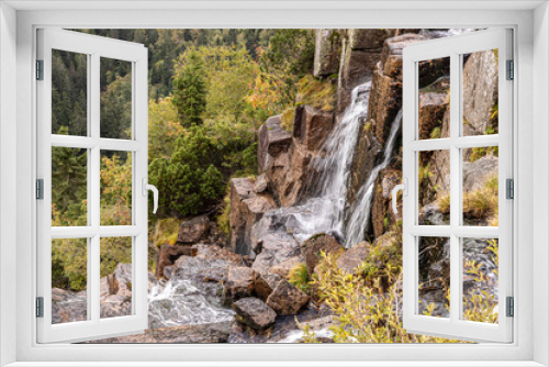 Fototapeta Naklejka Na Ścianę Okno 3D - Water falling over sharp square pieces of rock in the mountains. A brisk mountain stream. In the background coniferous forest and mountains Partly cloudy. Water in motion. Waterflow. Waterfall.