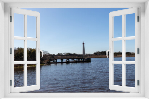 Fototapeta Naklejka Na Ścianę Okno 3D - I love the look of this beautiful lighthouse off in the distance. This is Cape May point lighthouse in New Jersey. The beautiful dock in front with smooth pond looks so pretty.