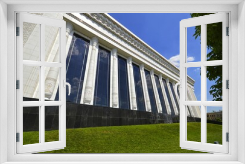 Fototapeta Naklejka Na Ścianę Okno 3D - A lawn and a white marble building with large Roman-style columns and dark reflective windows. Daytime urban landscape against a blue sky tree.