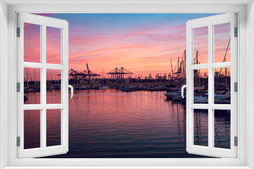 Fototapeta Naklejka Na Ścianę Okno 3D - Yachts with reflection in the sea water of the port of Valencia. Port cranes on the horizon. Warm evening in Spain.
