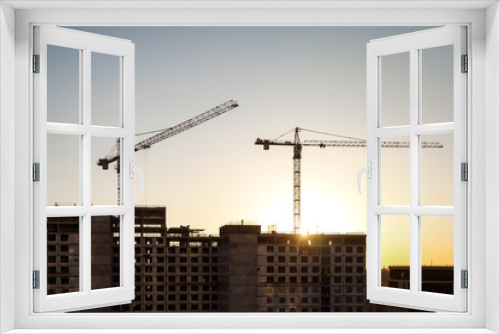 Fototapeta Naklejka Na Ścianę Okno 3D - Two industrial cranes on construction site house building at sunset sky background. Industry crane on creation site. Construction and renovation of buildings concept. Copy ad text space for banner