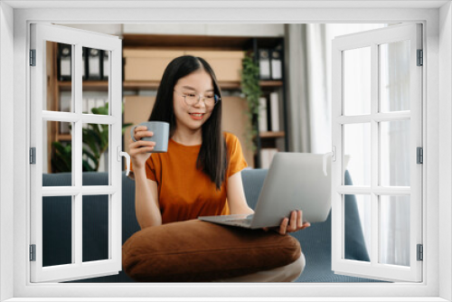 Female students note from the books at the Asian girl library sitting at the sofa using laptop computer and tablet to search an online informations.