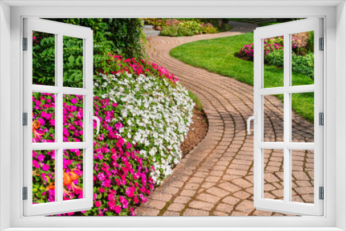 Fototapeta Naklejka Na Ścianę Okno 3D - Flowerbeds of vivid colored impatiens border a winding garden path.