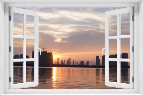 Fototapeta Naklejka Na Ścianę Okno 3D - The beautiful sunset view with the buildings' silhouette and orange color sky mirrored in the peaceful lake in the city