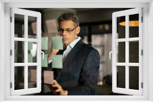 Portrait of successful businessman in office. Man writing ideas on colorful stickers on glass wall.